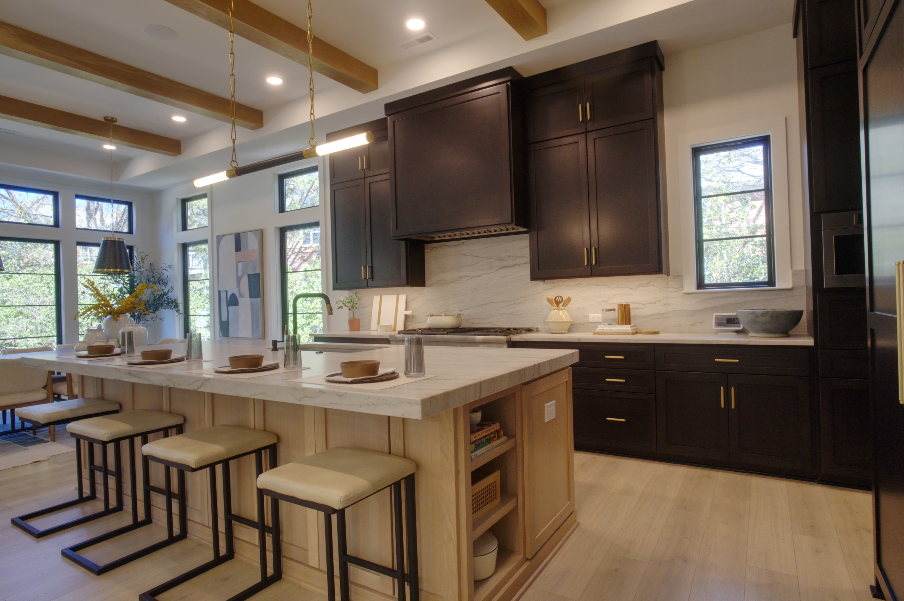 Modern kitchen with dark cabinetry, marble countertops, a large island, and wood ceiling beams.