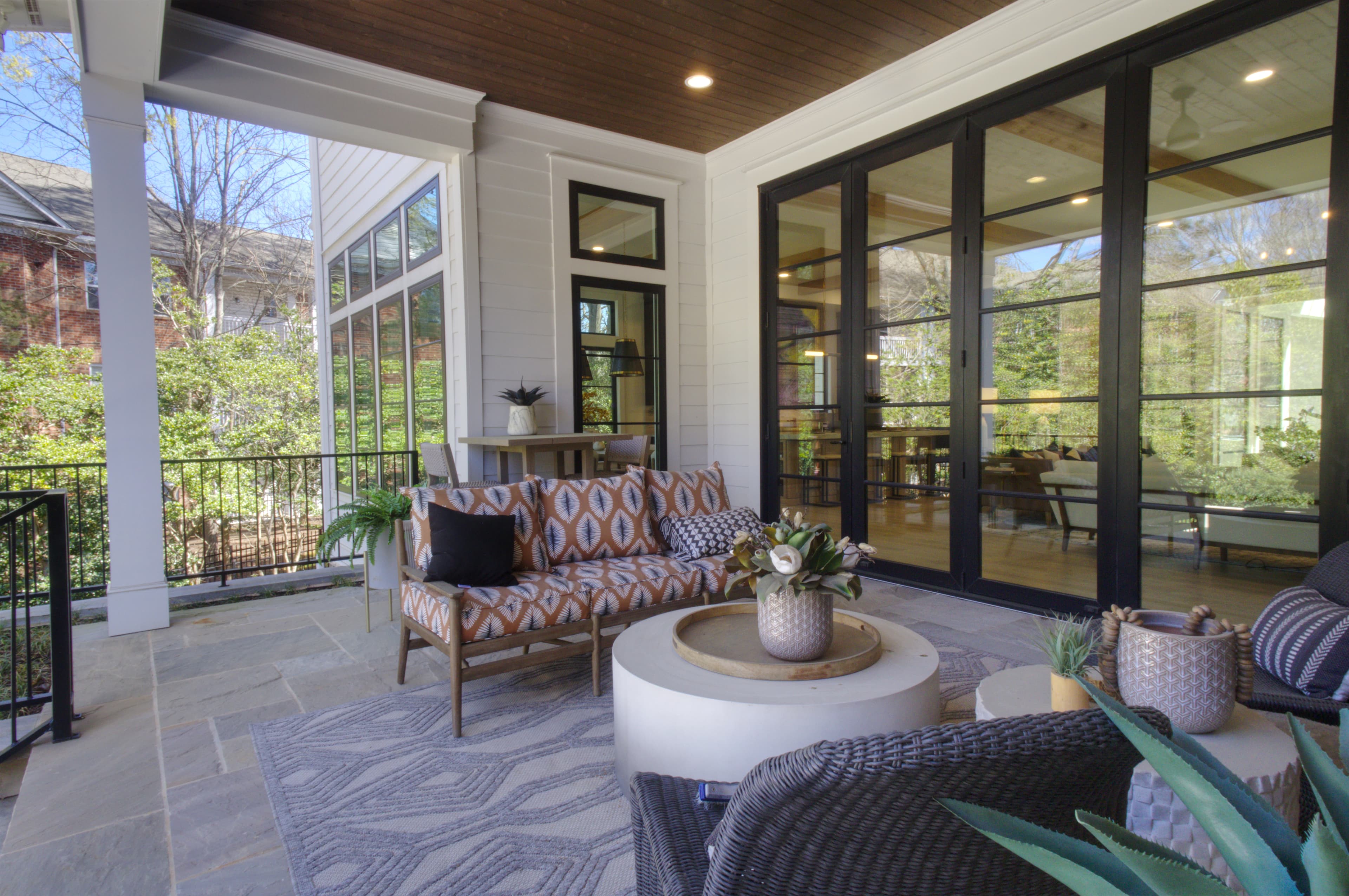 Modern covered patio featuring patterned sofa, round coffee table, and large black-framed glass doors.