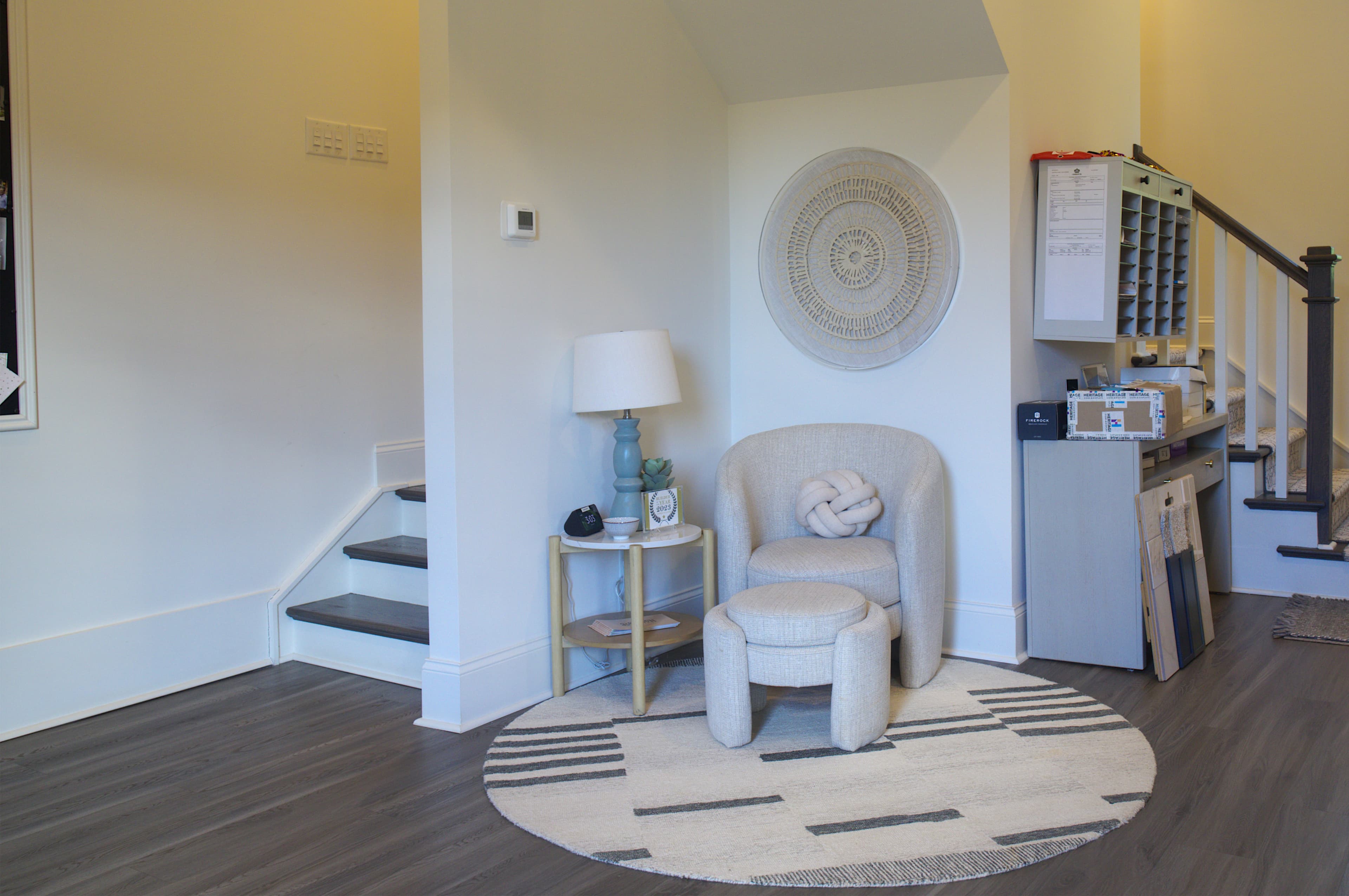 Cozy nook featuring a beige armchair, ottoman, round rug, and decorative circular wall art.