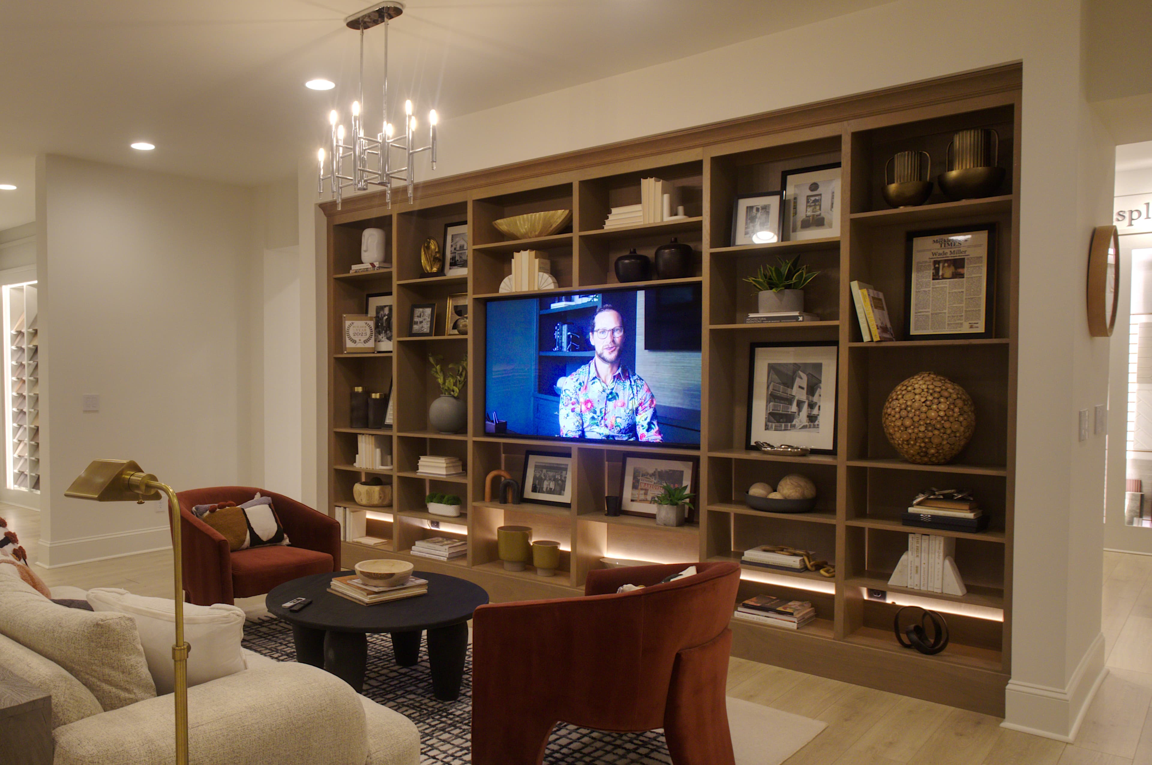 Modern living room with a large wooden built-in bookshelf, television, and two rust-colored armchairs.