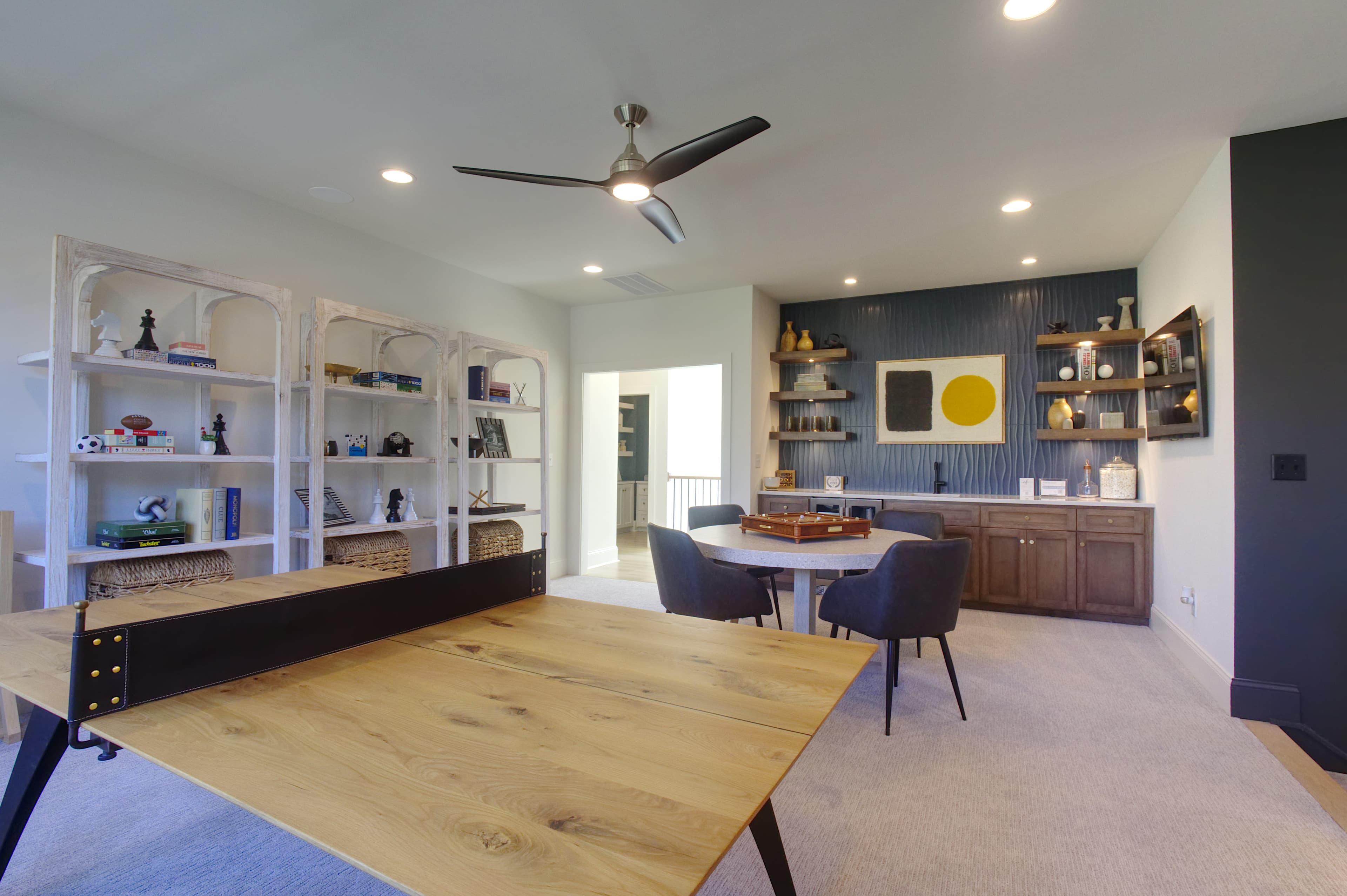 Modern game room with wooden ping-pong table, white shelving, and a blue textured wall.