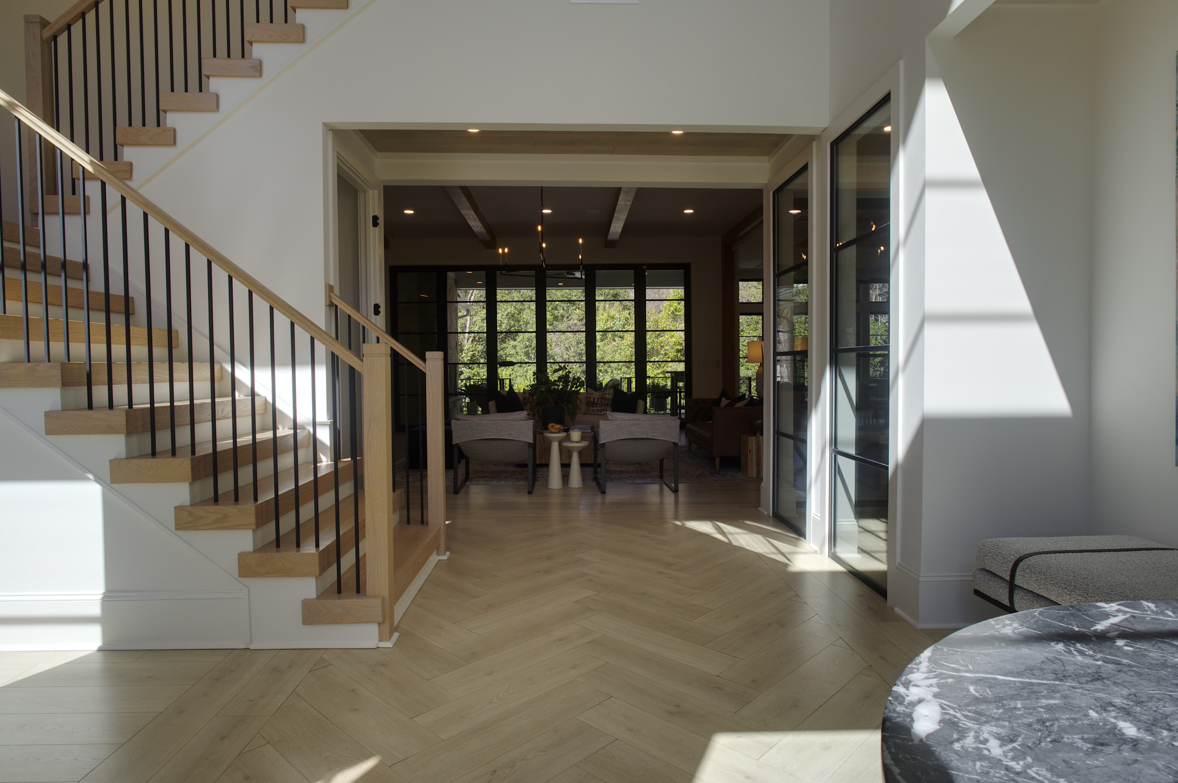 Modern home interior with herringbone floors, a wooden staircase, and a bright living area.