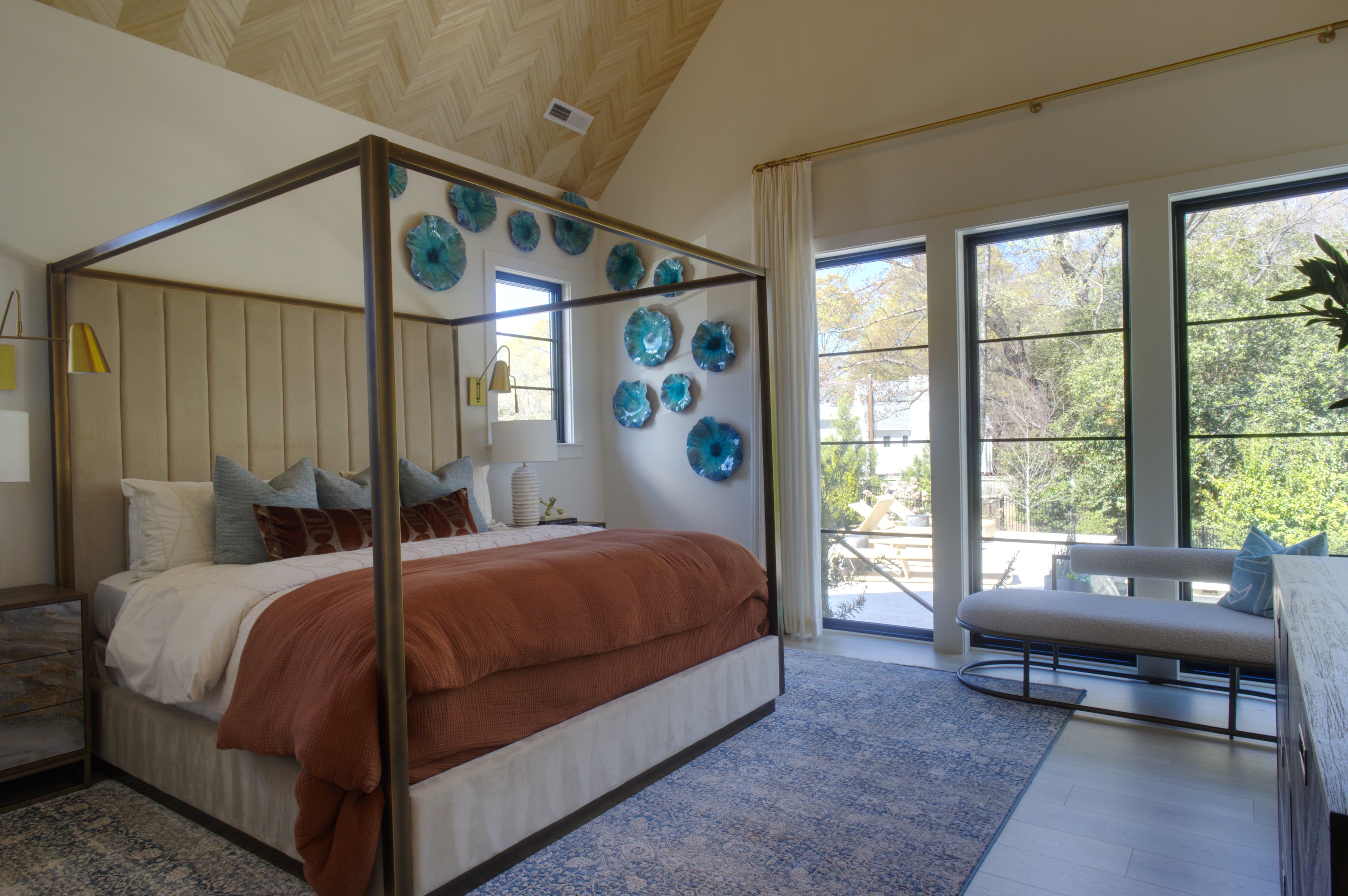 Modern bedroom featuring a brass four-poster bed, rust-colored duvet, and blue glass wall art.